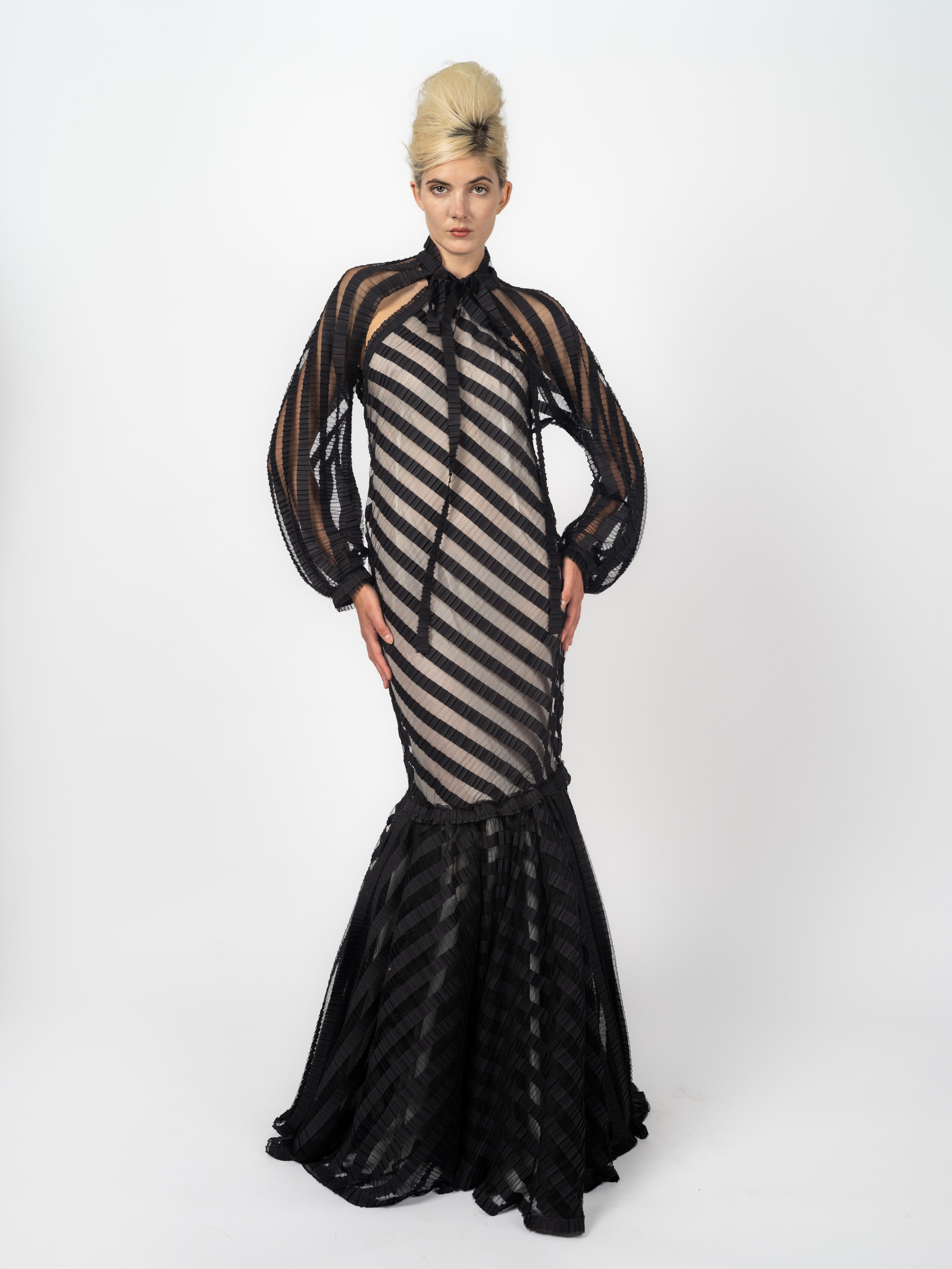 Transparentes Cape aus schwarzen Plissee-Streifen mit Ballonärmeln und Schleife, getragen über dem Neckholder-Abendkleid, von Maya Seyferth