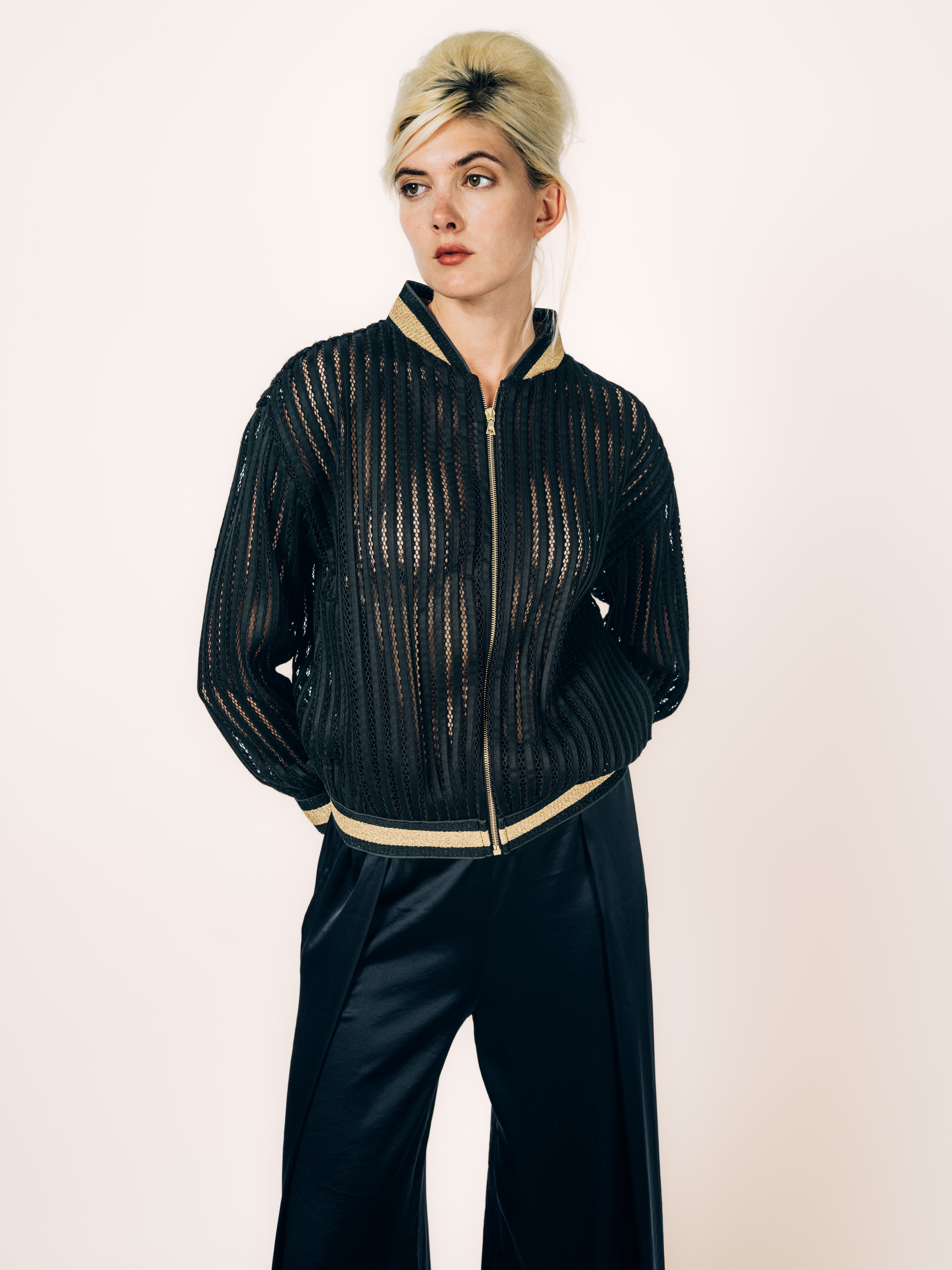 Bomberjacke Schwarz mit Netzstreifen und goldenen Bündchen, kombiniert mit schwarzer Seidenhose, von Maya Seyferth