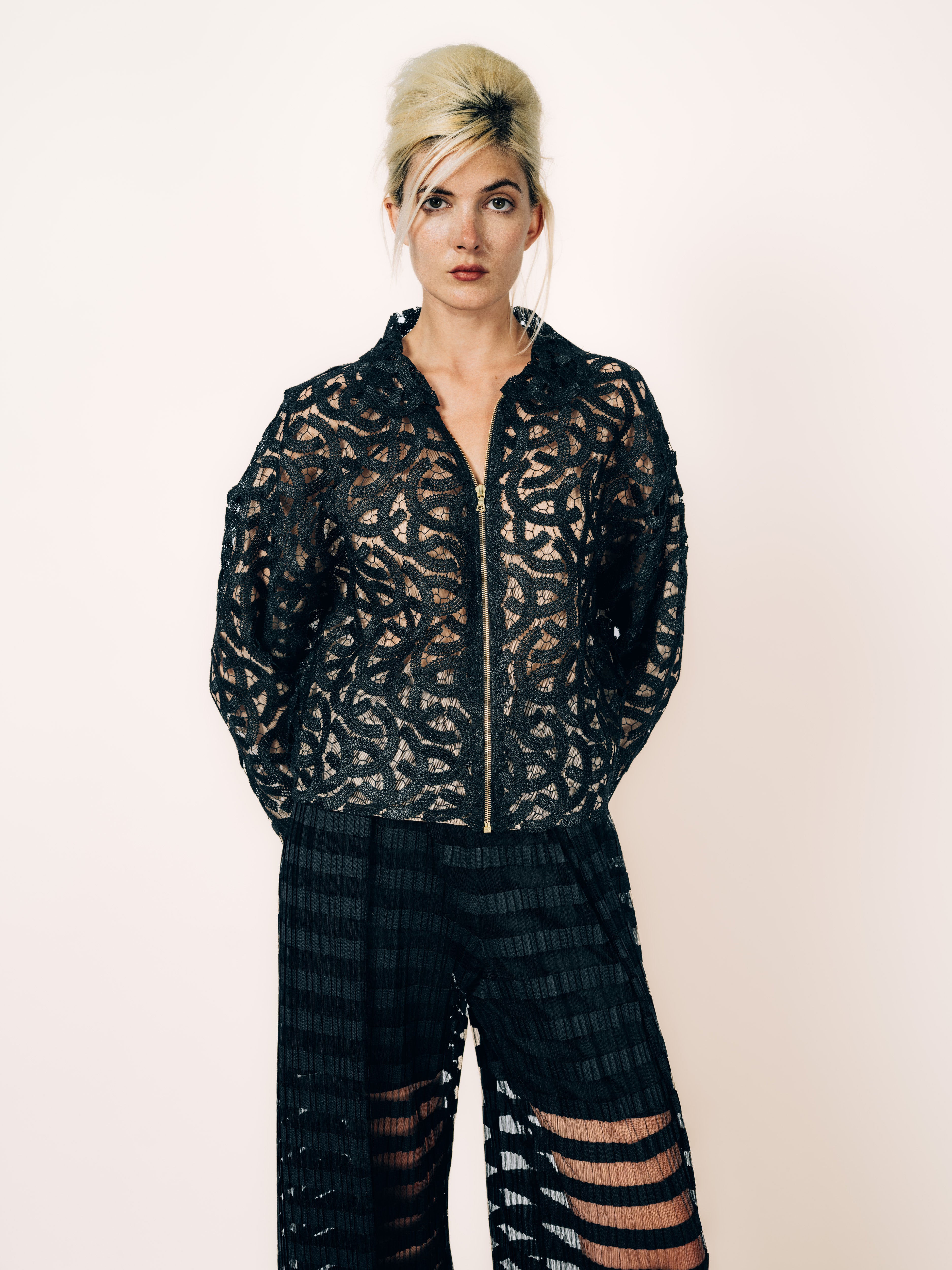 Bomberjacke Schwarz aus Spitze mit Ornamenten und weite schwarze Hose mit transparenten Plissee-Streifen von Maya Seyferth