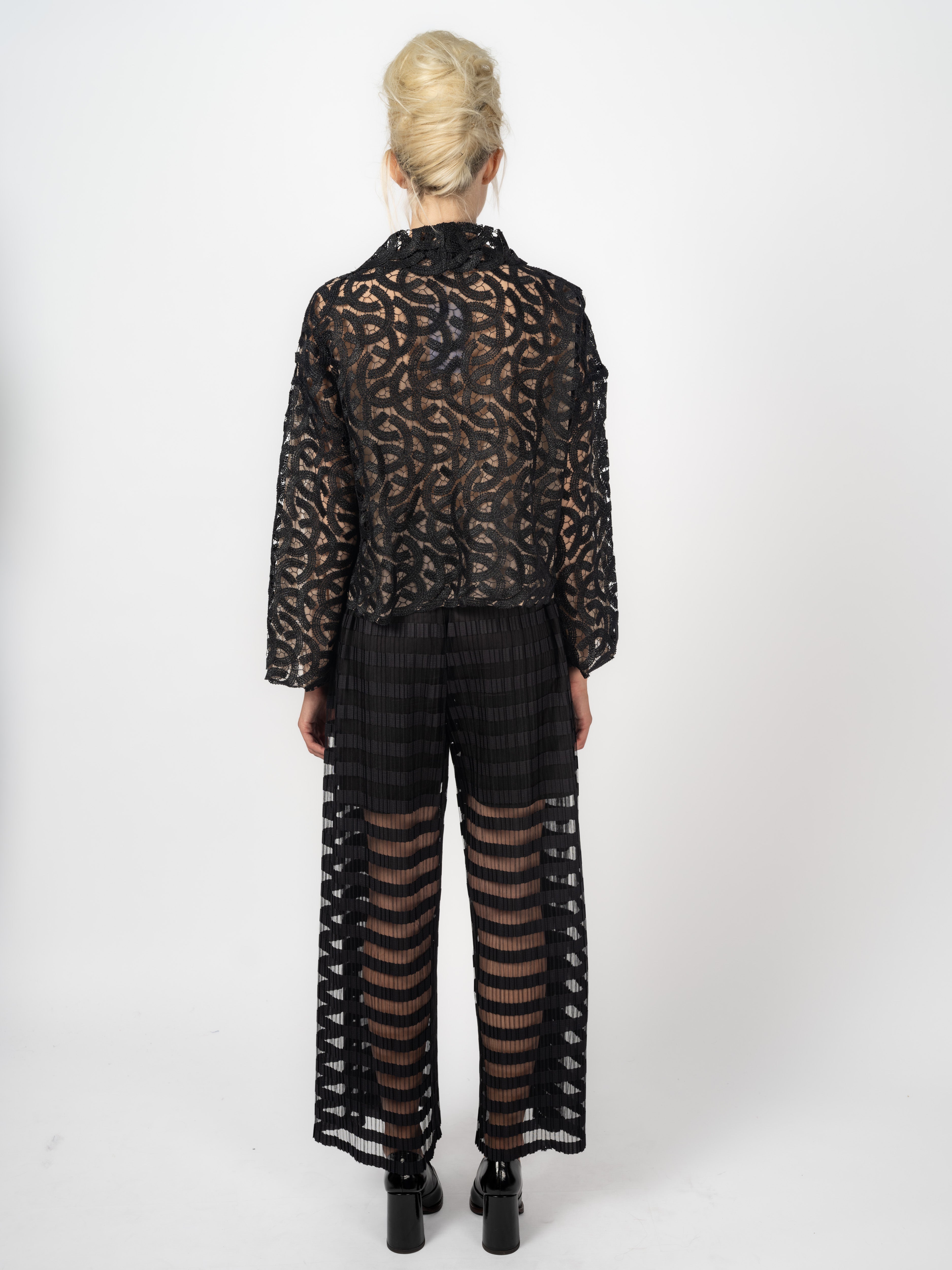 Bomberjacke Schwarz aus Spitze mit Ornamenten und weite schwarze Hose mit transparenten Plissee-Streifen von Maya Seyferth