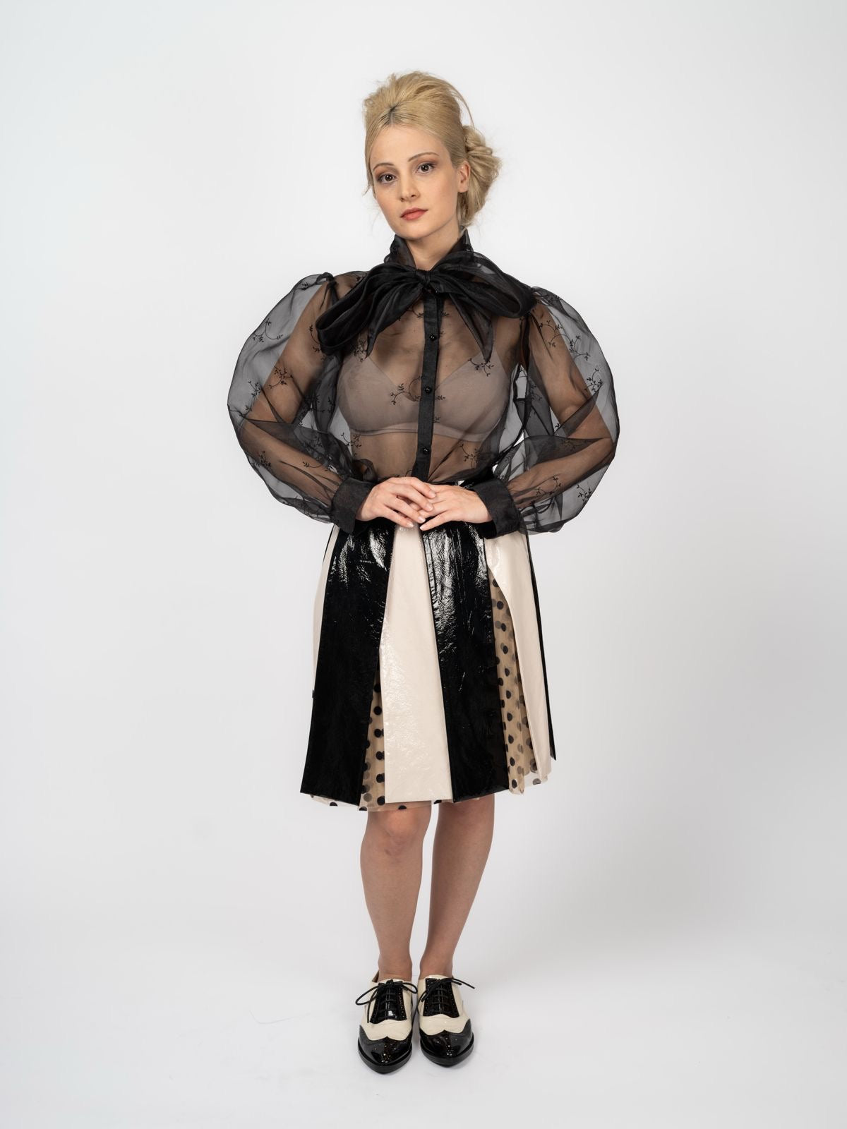 Schwarze Chiffon-Schluppenbluse mit feiner Stickerei und Rock in Schwarz und Creme mit gepunkteten Tülleinsätzen, dazu zweifarbige Schnürschuhe, von Maya Seyferth