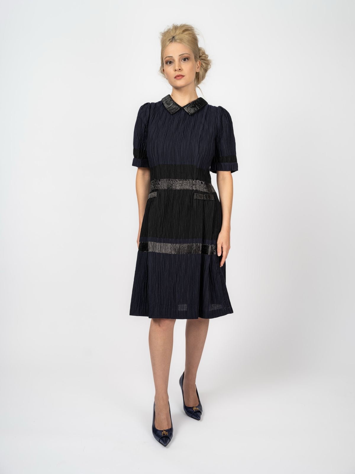 Knielanges Kleid in Marineblau und Schwarz mit Crinkle-Struktur, Bubikragen und glänzenden Bändern, dazu marineblaue Pumps, von Maya Seyferth